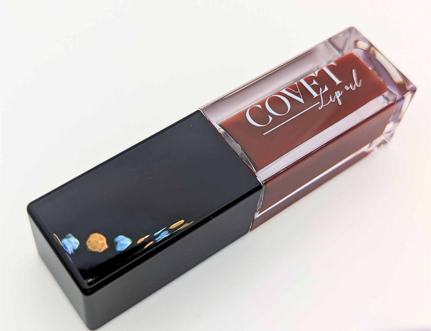 Covet Hazelnut Cream lip gloss angled on a white background, showing a rich brown gloss in a clear tube with glossy black cap.