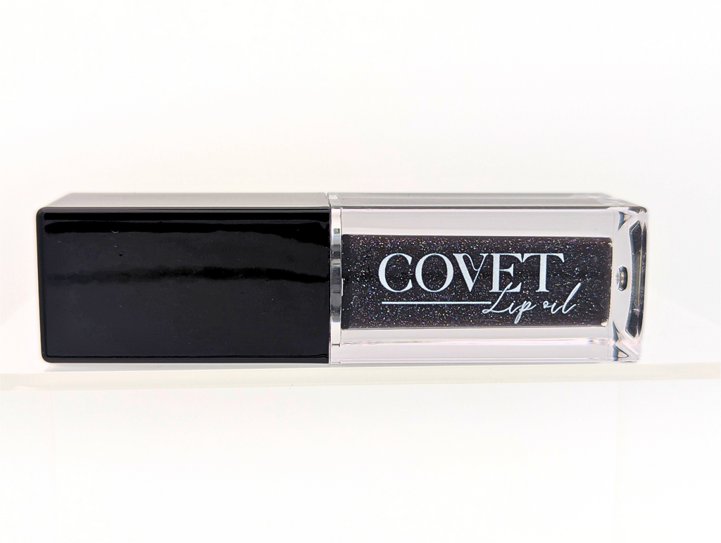 Covet Beauty’s Black Currant lip gloss — a deep black-violet gloss with shimmer in a clear rectangular tube with black cap. Transforms into a rich plum based on skin pH and heat.