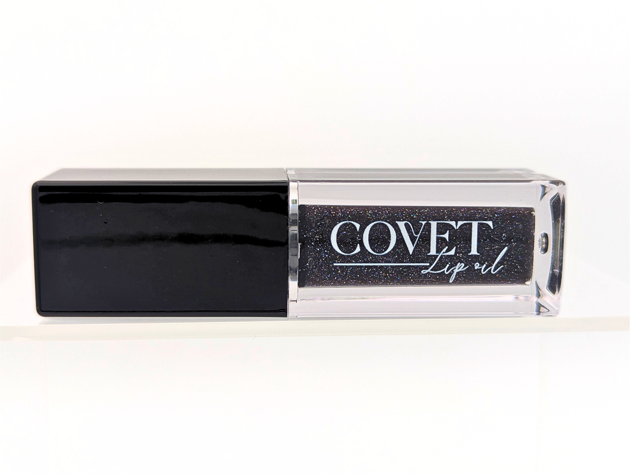 Covet Beauty’s Black Currant lip gloss — a deep black-violet gloss with shimmer in a clear rectangular tube with black cap. Transforms into a rich plum based on skin pH and heat.