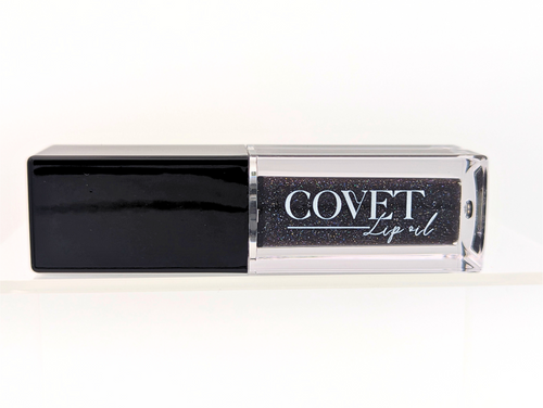 Covet Beauty’s Black Currant lip gloss — a deep black-violet gloss with shimmer in a clear rectangular tube with black cap. Transforms into a rich plum based on skin pH and heat.
