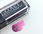 Covet Beauty Black Currant lip gloss — a deep black-violet gloss with subtle iridescent shimmer that blooms into a cool berry flush, shown swatched after 30 seconds on a white background