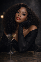 Woman in a black dress and gloves holding a cocktail glass against a dark background, wearing Covet No. 4 Melt.