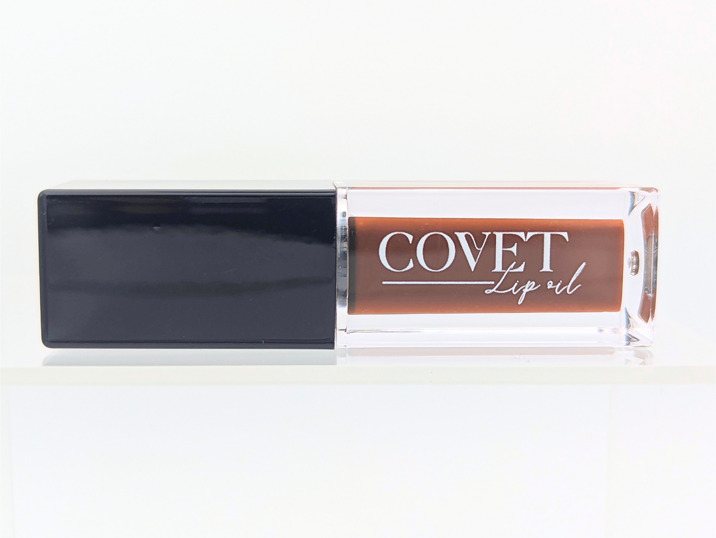 Front-facing image of Covet Lip Oil in Chocolate Cookie, featuring the clear tube and dark cap against a crisp white background.