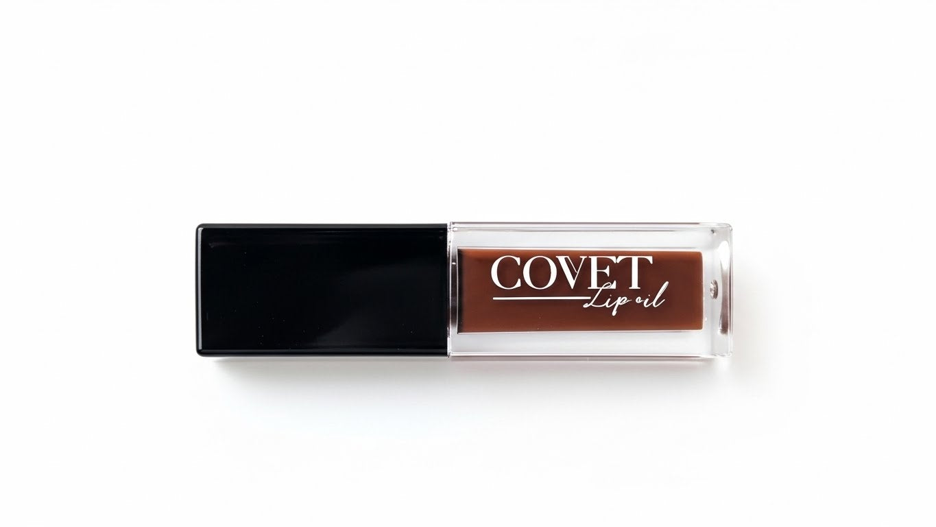 A Covet Lip Oil in a sleek rectangular tube with a black cap and clear base, filled with a warm cocoa-brown shade, photographed against a bright white background.