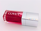 Angled view of ‘Crave’ lip gloss by Covet Beauty, showing its cool raspberry hue and glass-like shine. The tube catches soft light on a white surface, highlighting its smooth, reflective texture