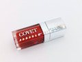 Angled view of ‘Melt’ lip gloss by Covet Beauty, showing its warm terracotta hue and smooth, mirror-like shine. The clear tube reflects light gently on a white surface, emphasizing its rich, glossy texture
