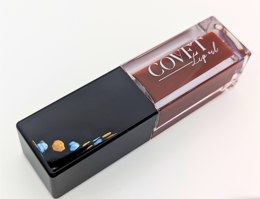 Covet Hazelnut Cream lip gloss angled on a white background, showing a rich brown gloss in a clear tube with glossy black cap.