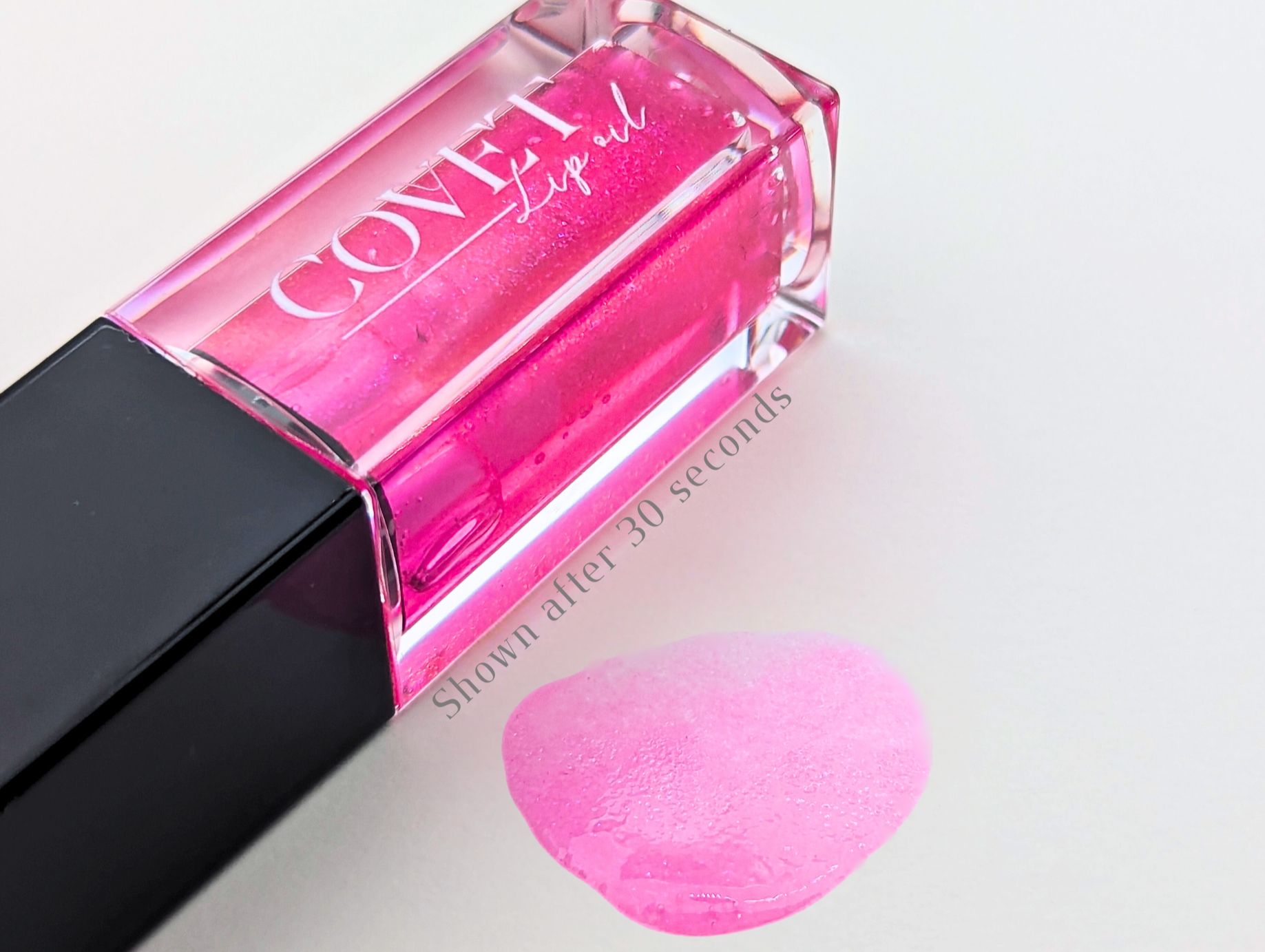 Covet Beauty Jupiter lip gloss — bold hot pink gloss with violet shimmer, shown in a clear square tube and swatched on a white background 30 seconds after application.