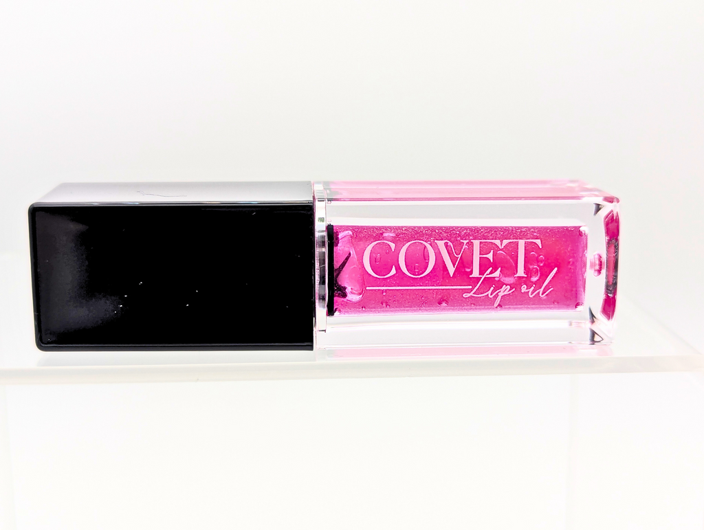 Covet Beauty’s Jupiter lip gloss — a bold fuchsia gloss in a clear rectangular tube with black cap. Transforms into a vivid cool pink based on skin pH and heat.
