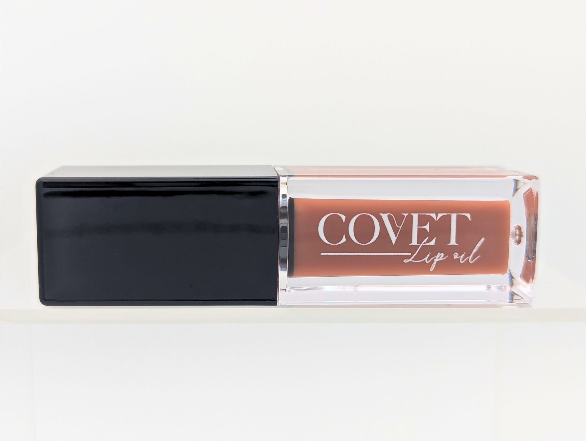 Covet Latte Cream lip gloss on a white background showing the soft beige tone inside a clear tube with black cap