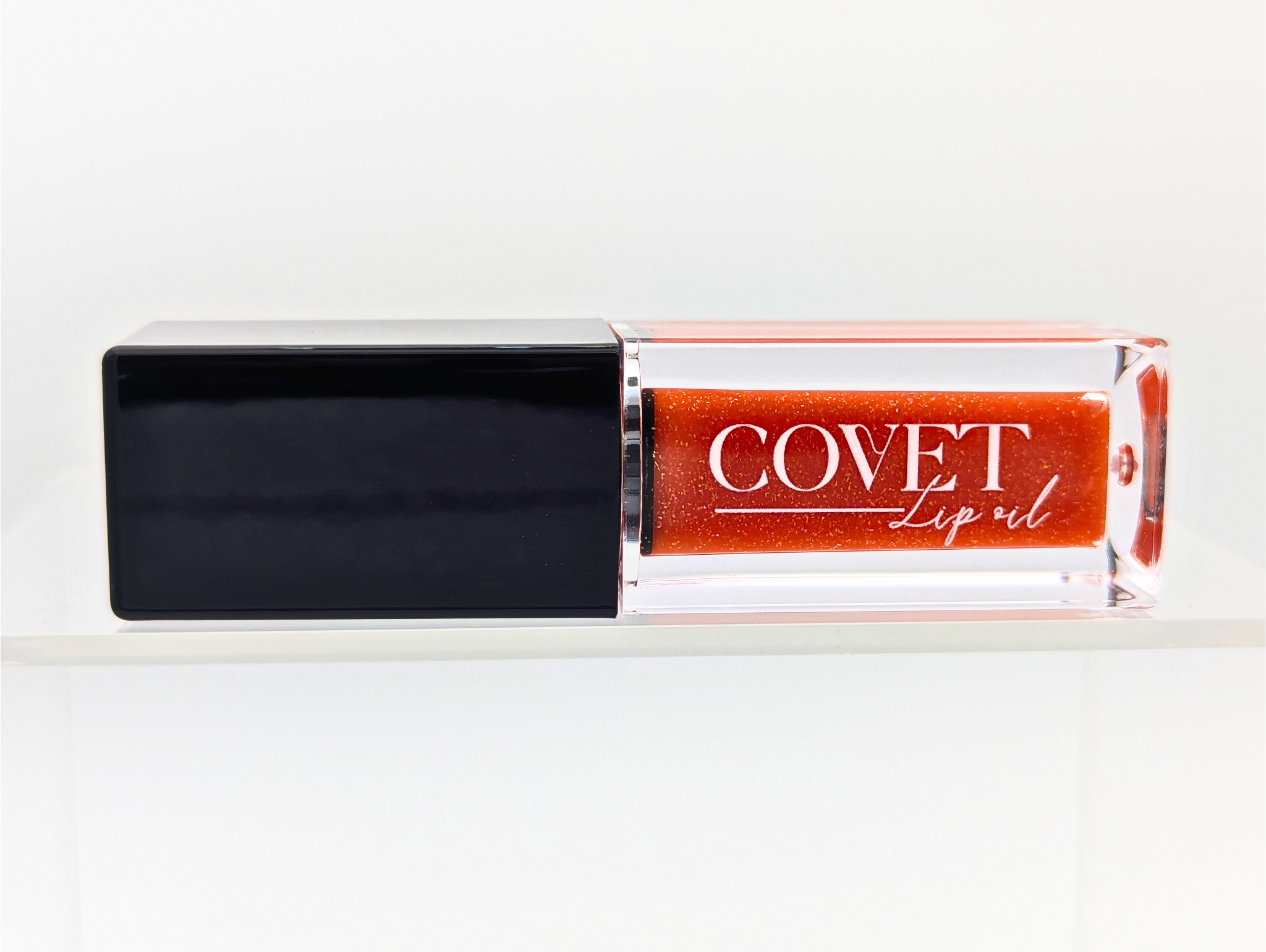 Covet Beauty’s Mars – Rust Bloom lip gloss stain— a vibrant orange gloss in a rectangular tube with black cap. Transforms into a soft coral pink based on skin pH and heat.