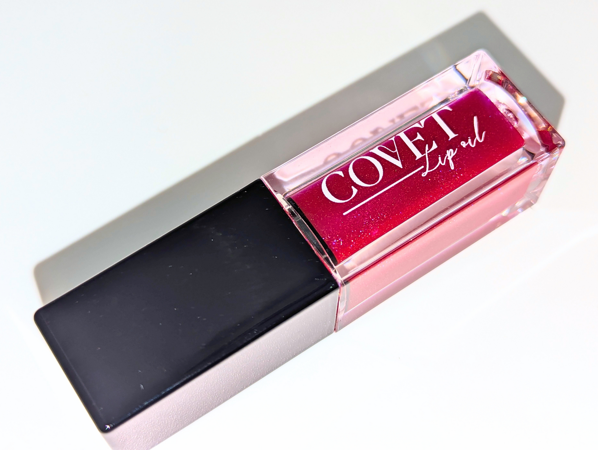 Covet Maple Love lip gloss angled on a white background, revealing golden-red shimmer in a rich crimson gloss.
