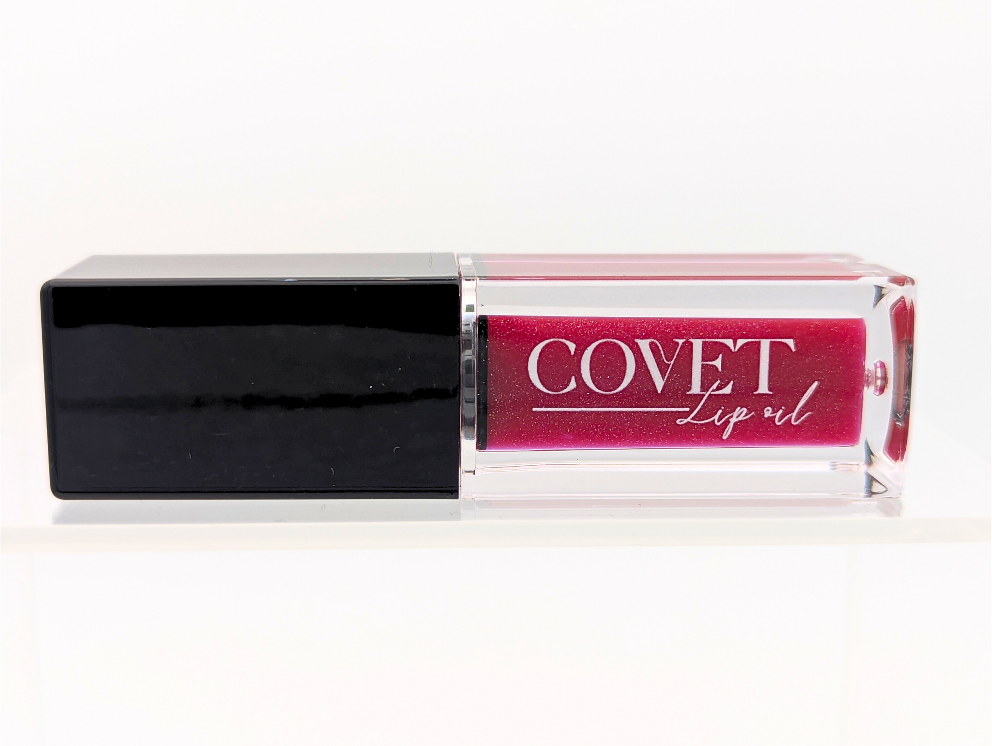 Covet Maple Love lip gloss front-facing in its clear packaging, highlighting the deep red hue with subtle shimmer.