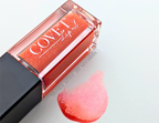 ovet Beauty Mars lip gloss — warm coral-orange gloss with fine gold shimmer, shown in a clear square tube and swatched on a white background after 30 seconds of bloom.