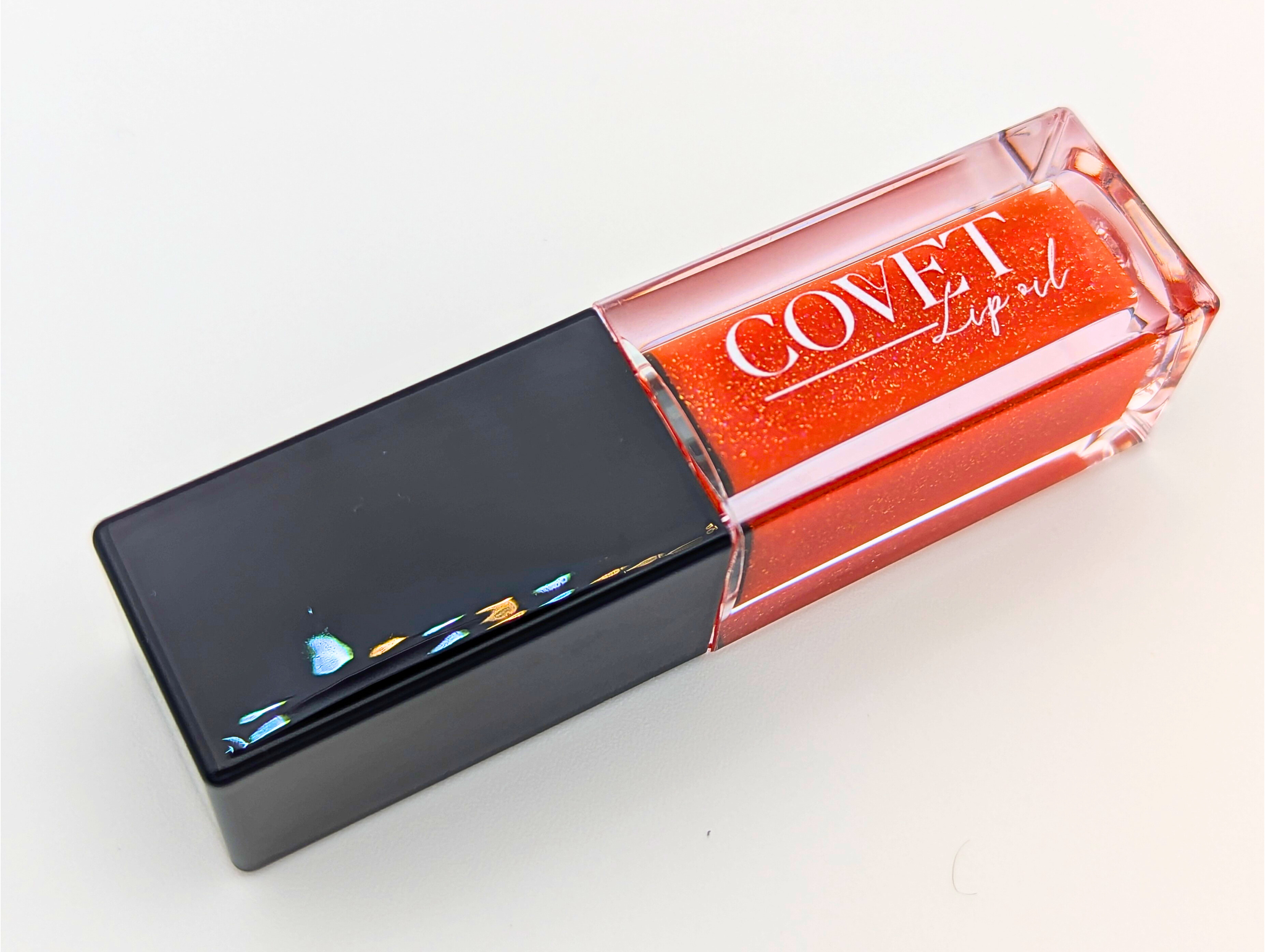 Covet Beauty’s Mars – Rust Bloom lip gloss stain— a vibrant orange gloss in a rectangular tube with black cap. Transforms into a soft coral pink based on skin pH and heat.