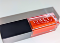 Covet Beauty’s Mars – Rust Bloom lip gloss stain— a vibrant orange gloss in a rectangular tube with black cap. Transforms into a soft coral pink based on skin pH and heat.