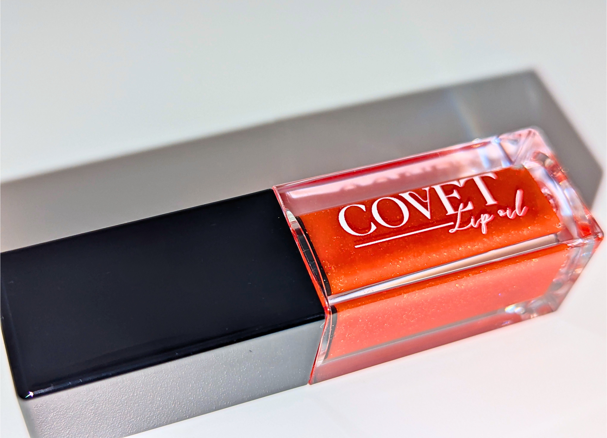 Covet Beauty’s Mars – Rust Bloom lip gloss stain— a vibrant orange gloss in a rectangular tube with black cap. Transforms into a soft coral pink based on skin pH and heat.