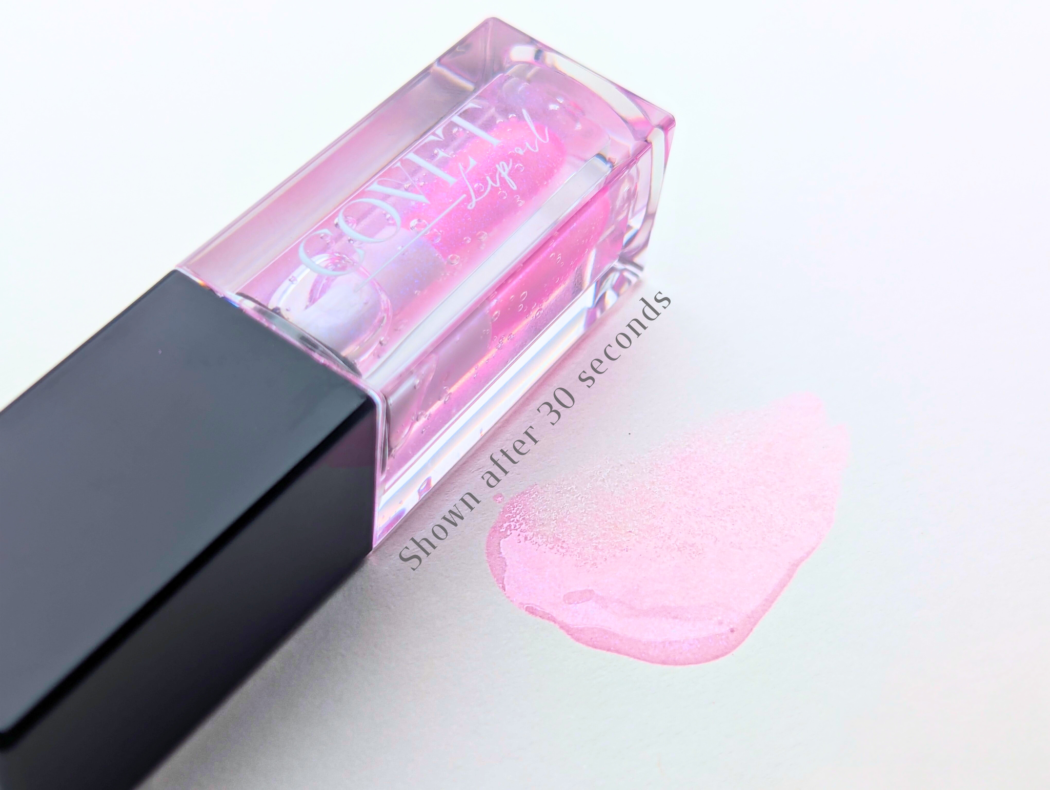 Covet Beauty Ocean of Stars lip gloss — sheer pink gloss with violet and pearl shimmer, shown in a clear square tube and swatched on a white background after 30 seconds of activation