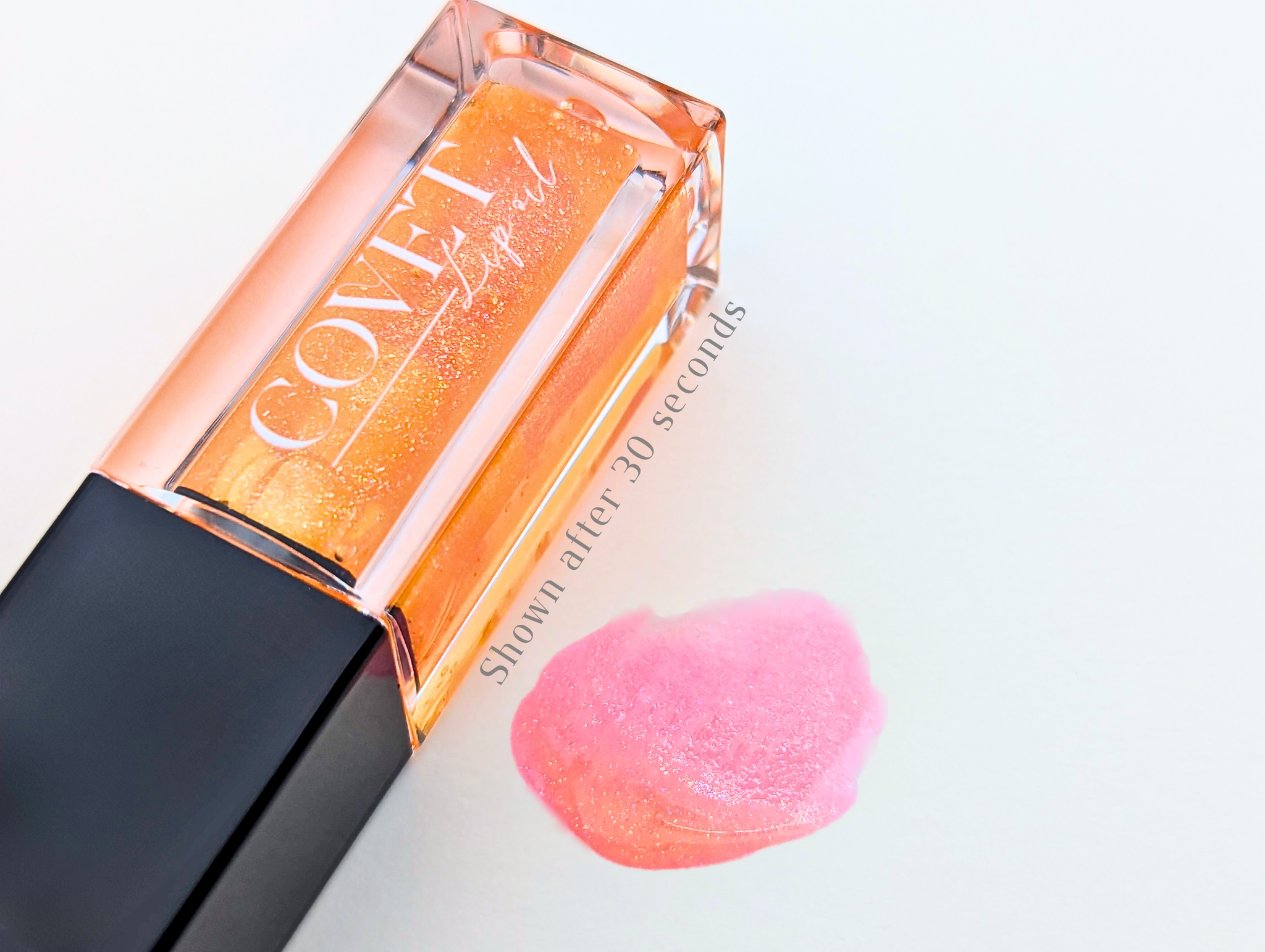 Covet Beauty Saturn lip gloss — a vivid orange gloss with golden shimmer that blooms into a coral-pink shade after application, shown swatched on a white background after 30 seconds.