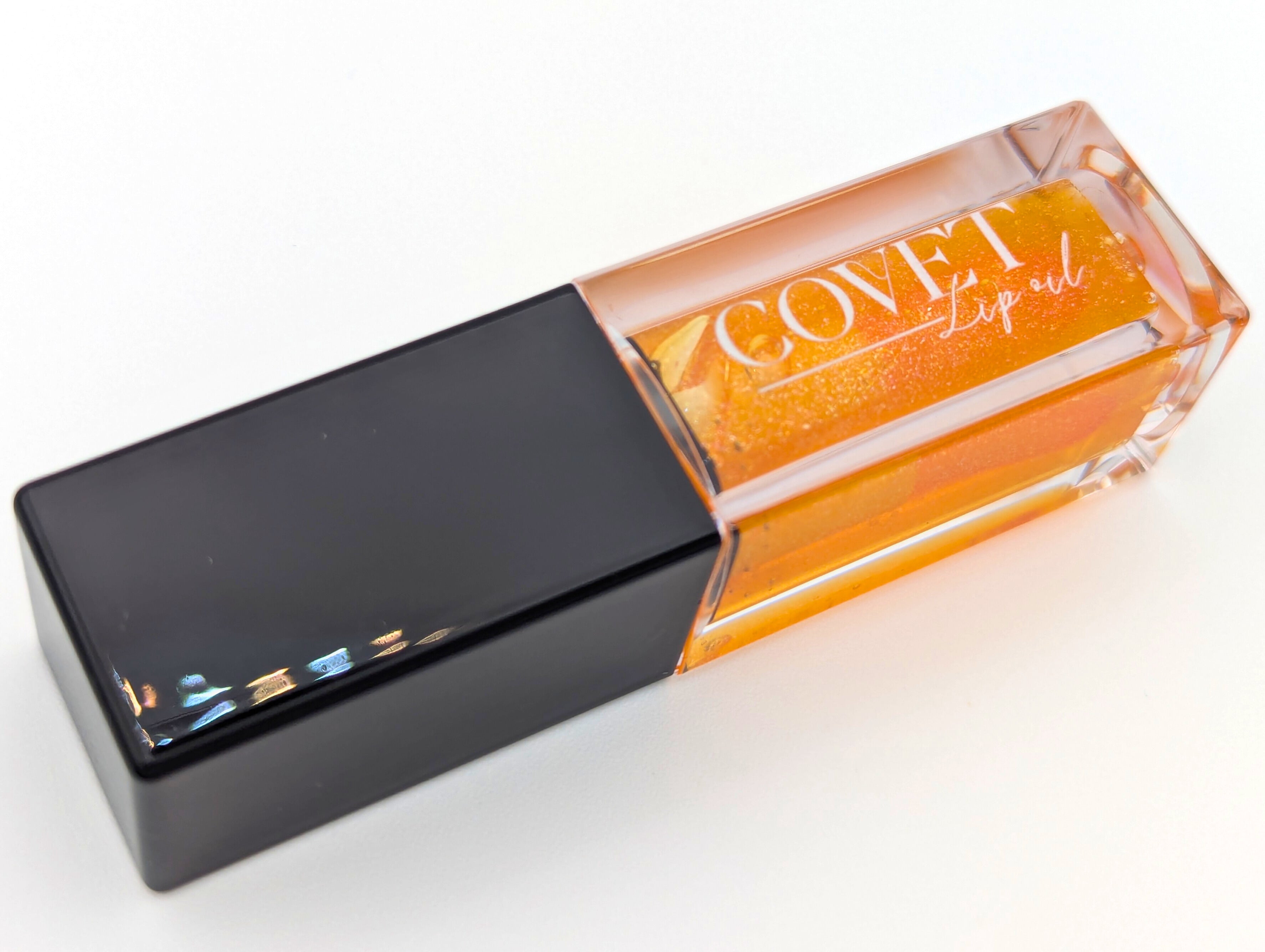 Covet Beauty’s Saturn lip gloss — a shimmering orange gloss in a clear rectangular tube with black cap. Transforms into a soft rose pink based on skin pH and heat.