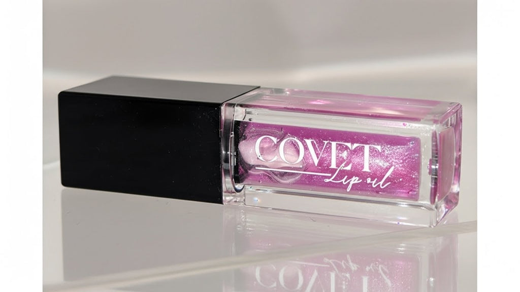 A Covet Lip Oil in a clear rectangular tube with a black cap, filled with a shimmering violet-pink shade, photographed on a glossy white surface with soft, diffused lighting.