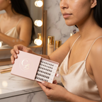 Covet Beauty Veil cluster lashes shown in an open pink tray held near a vanity mirror.