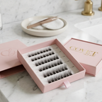 Covet Beauty Trance cluster lashes displayed in an open pink tray with soft packaging on a marble vanity.