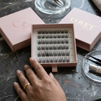 Covet Beauty Hush cluster lashes shown in an open lash tray with pink packaging on a marble surface.