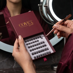 Model holding Covet Beauty Velvet cluster lashes in burgundy packaging while selecting a lash cluster with tweezers.